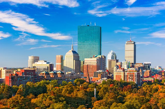 Skyline of Boston on a sunny day with trees in the foreground.