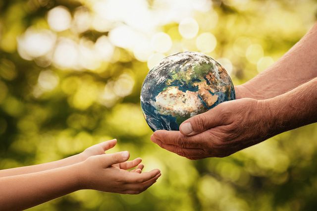 Conceptual photograph of an older person handing the earth to a younger person.