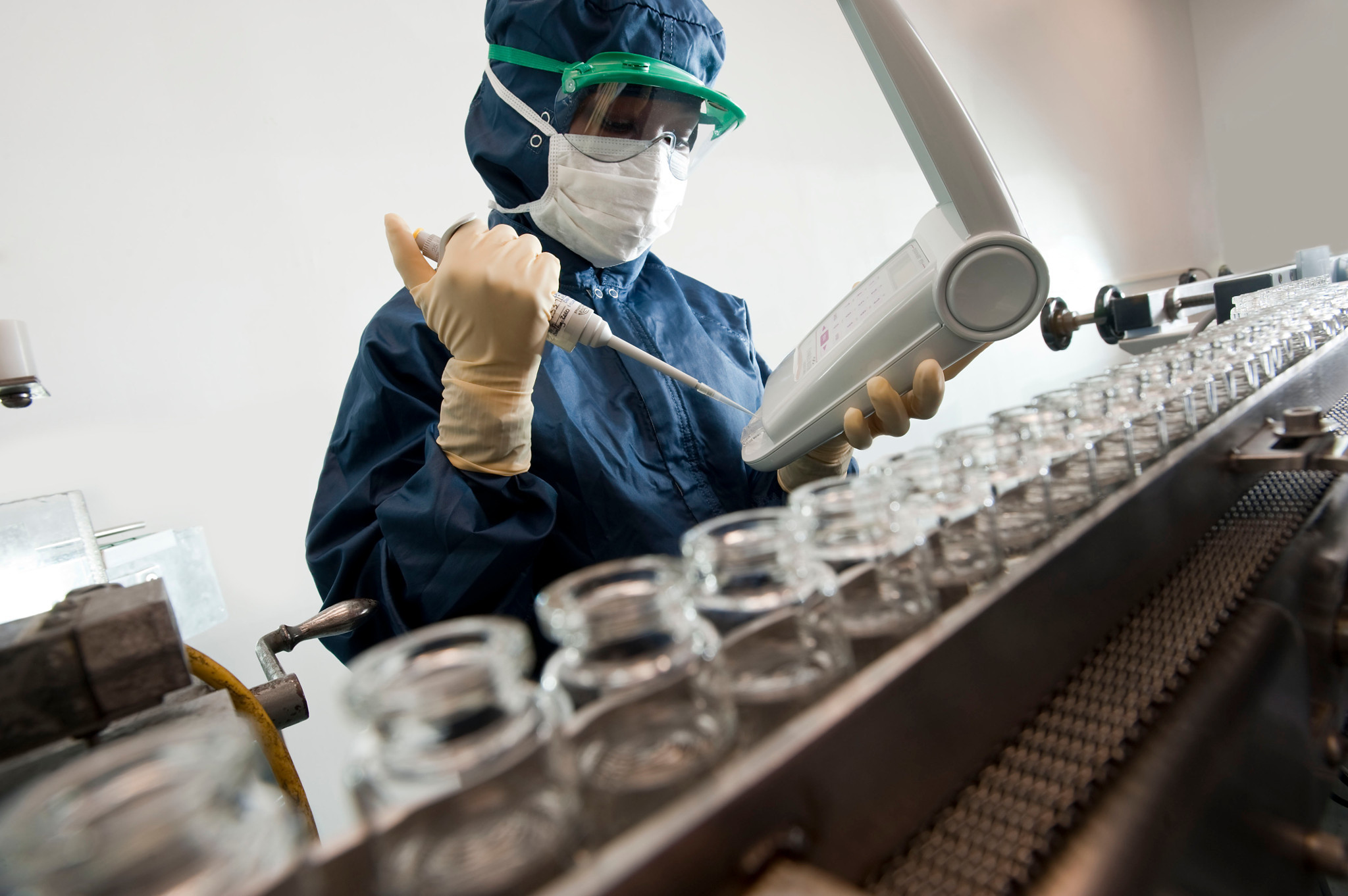 Scientist wearing full PPE using a pipette in a lab.