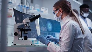 Scientist in a lab looking at a microscope conducting GLP-validated peer review.