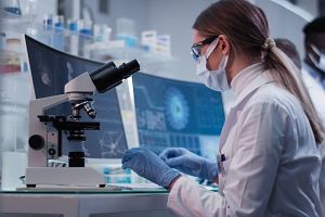Scientist in a lab looking at a microscope conducting GLP-validated peer review.