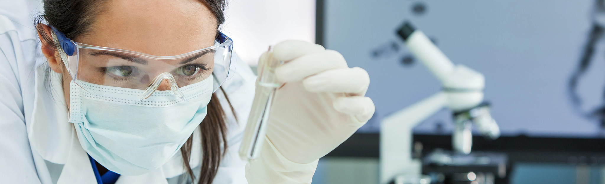 Female scientist examining a test tube with a clear solution in a lab.