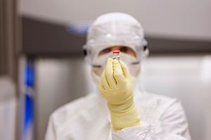 Scientist wearing PPE and holding a vial.