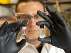 close up of scientist holding a small vial in each hand with black gloves on