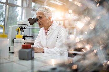 Scientist looking through a microscope in a cell and gene therapy lab.