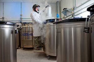 scientist wearing PPE removing media from a cell storage tank