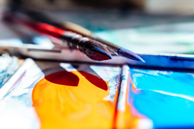 Photograph of paintbrushes with paint on them, lying over a palette of paint.