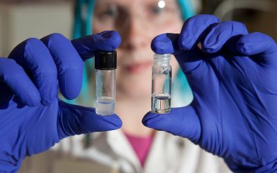 close up of scientist holding a small vial in each hand with blue gloves on