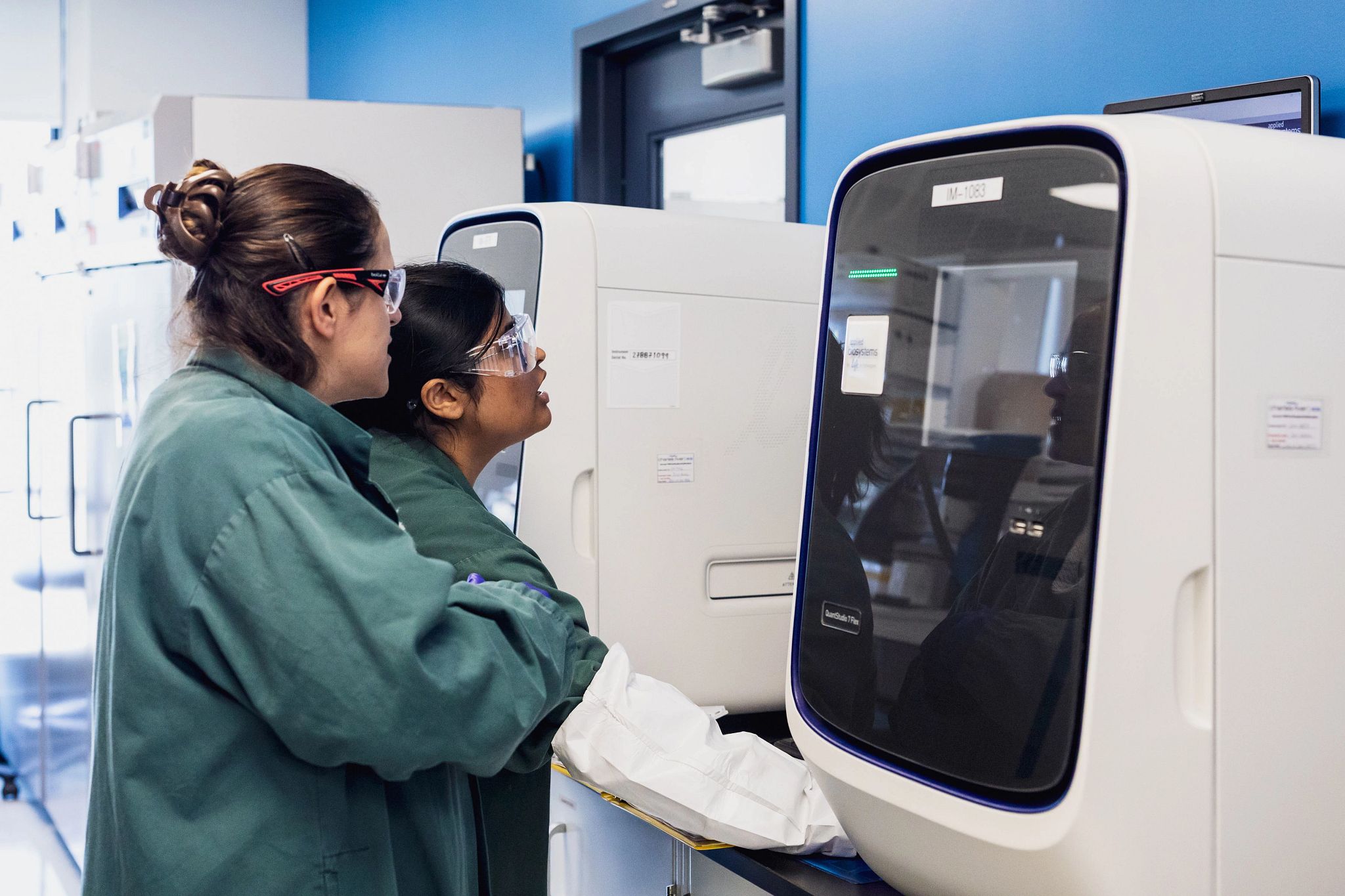 Two individuals operating laboratory sequencing machines in a research lab, molecular biology services underway within a specialist lab