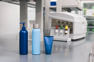 Cosmetic bottles and tube on a lab bench with microbiology testing equipment in the background, representing quality control in home and personal care manufacturing