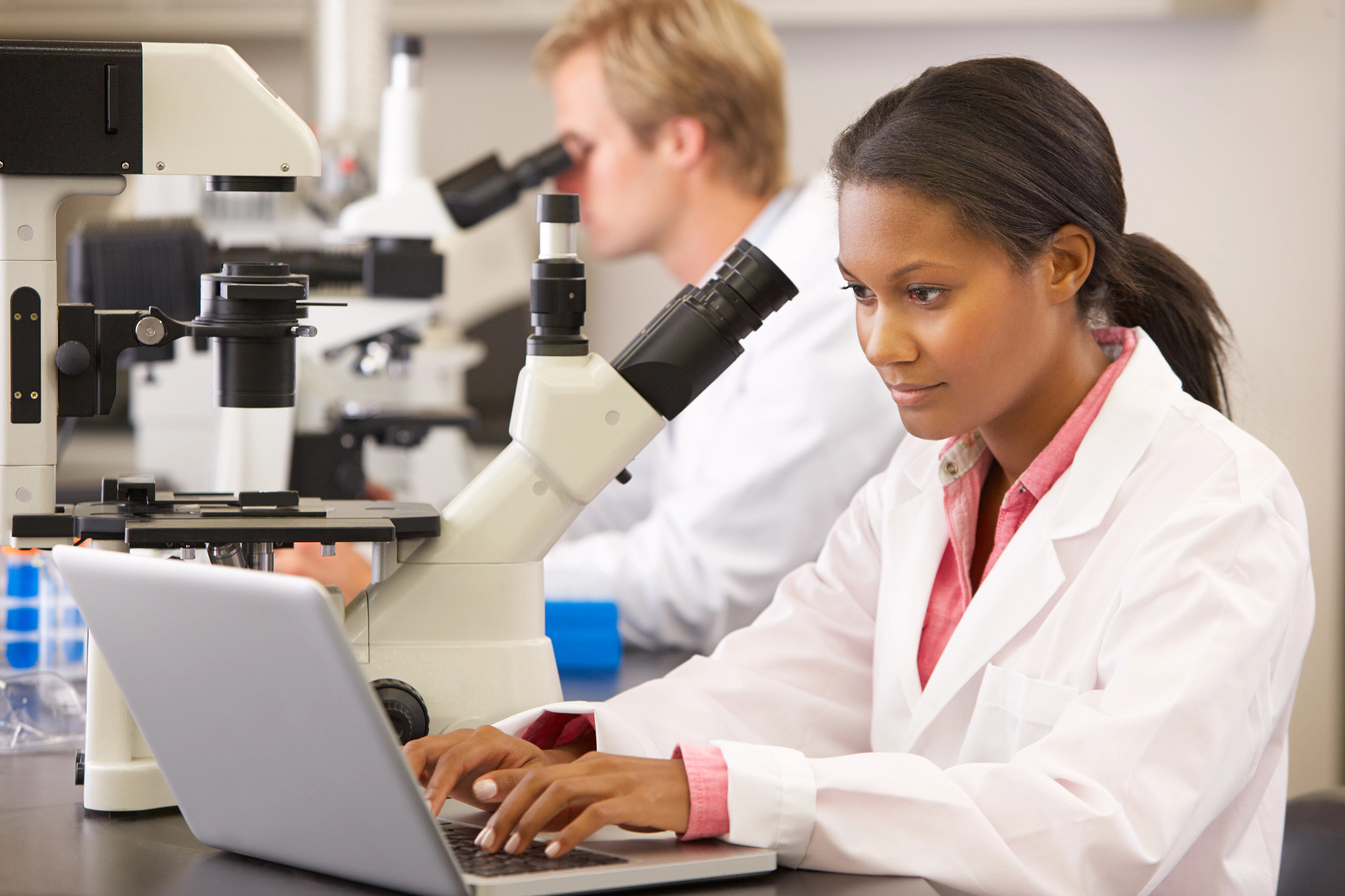 Male And Female Scientists Using Microscopes and Laptop In Laboratory