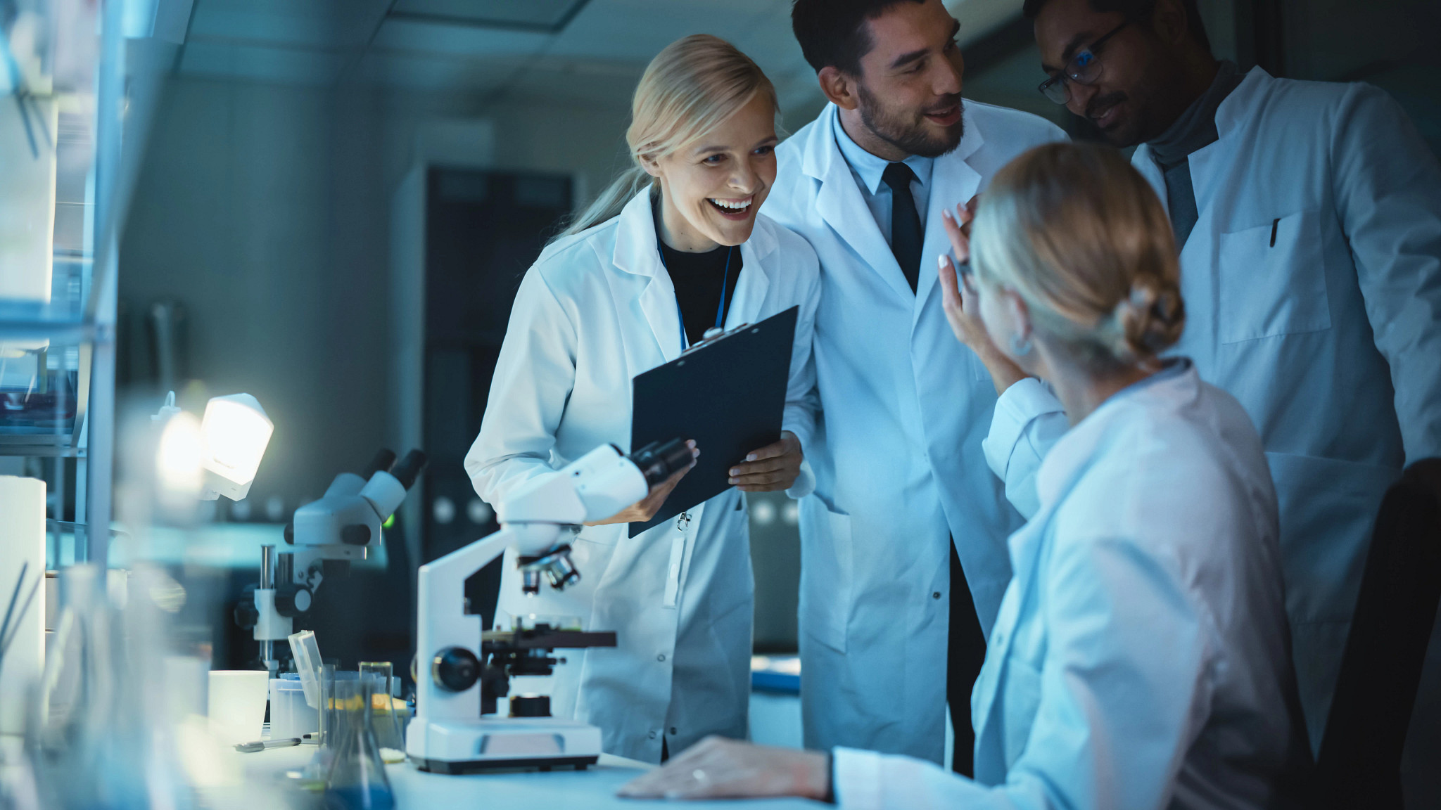 Nonclinical safety assessment research scientists wearing lab coats celebrate success with fellow bioengineers.