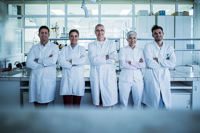 five smiling scientists in lab coats standing in a lab