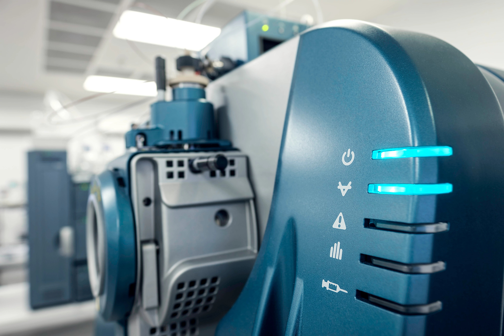 Close-up view of a laboratory mass spectrometer, focusing on its control panel with illuminated indicator lights and symbols for power, alerts, and operational status.