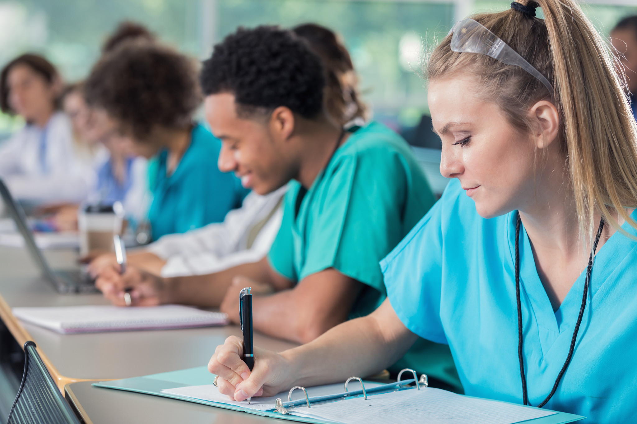 students wearing scrubs taking notes in a training class