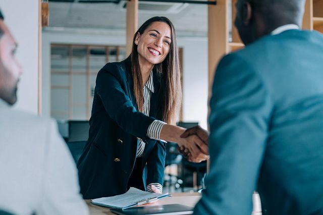 Photo of a young woman shaking hands with a man over a desk.