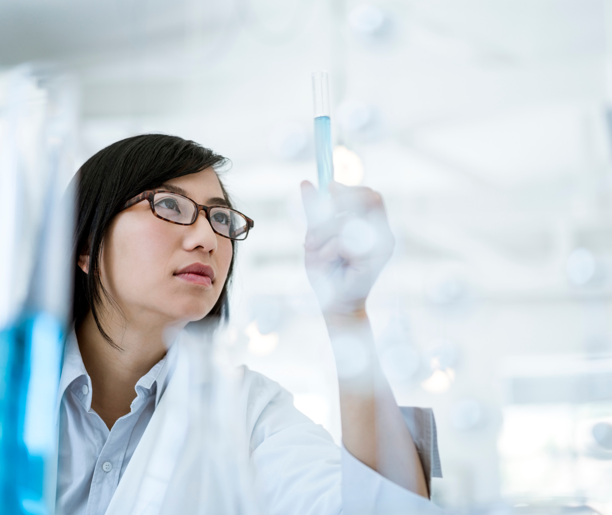 Scientist with glasses in a lab coat looking at a test tube full of blue liquid.