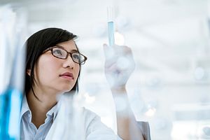 Scientist with glasses in a lab coat looking at a test tube full of blue liquid.