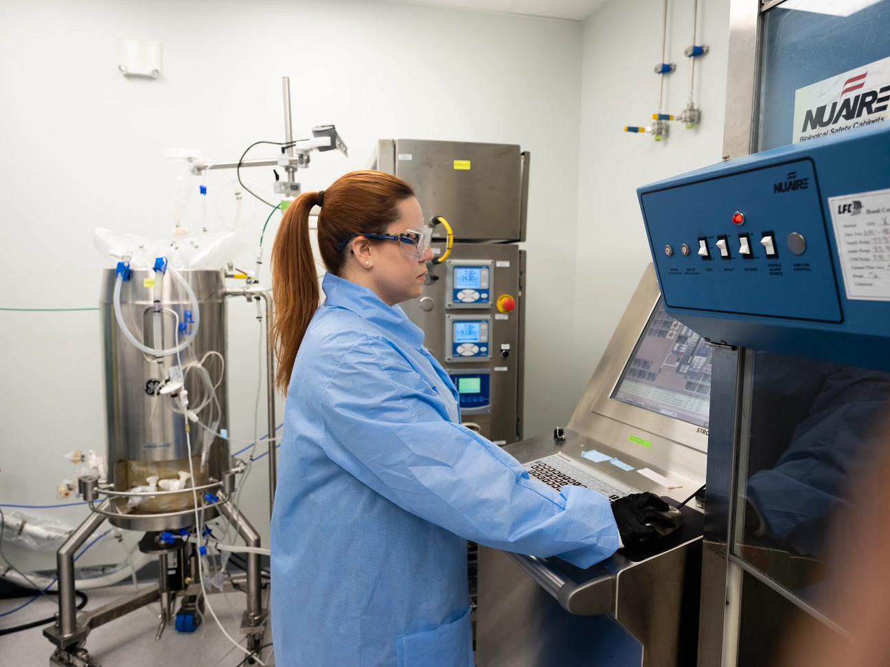 Person in a blue lab coat operates equipment in a cleanroom operates a 50L bioreactor at Charles Riverâs Viral Vector CDMO Center of Excellence