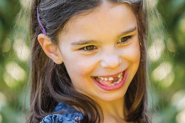 Photo of a young girl named Mila. She is smiling and looking to the side of the camera.