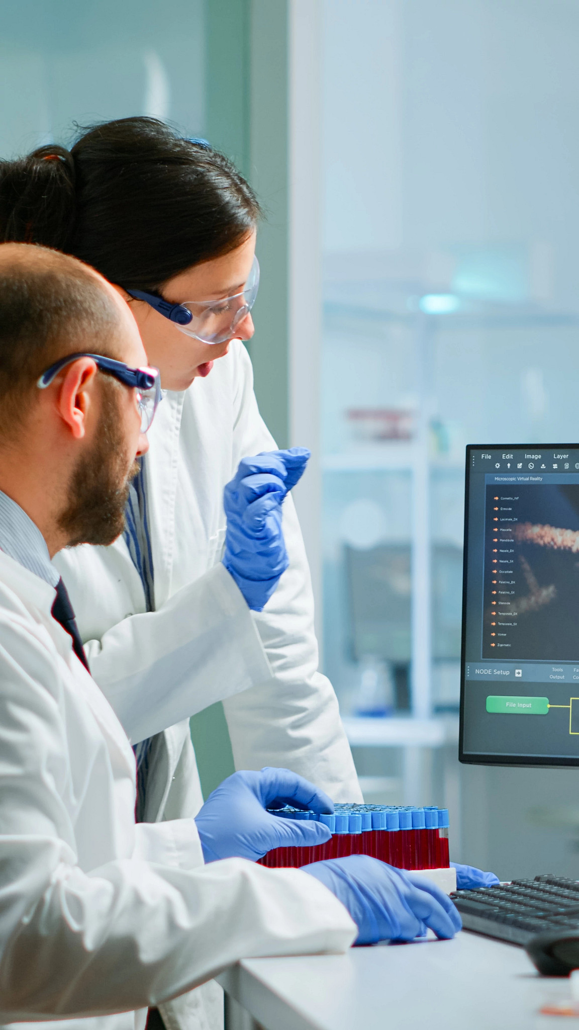 Team medical scientist conducting DNA experiments looking in computer holding test tube with blood sample working in science laboratory.