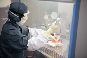 Technican wearing full PPE working with a pipette in a flow hood